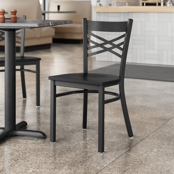 A black Lancaster Table & Seating cross back chair with a black wood seat at a table in a restaurant.