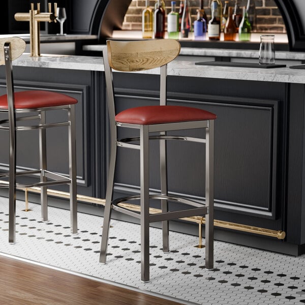 Two Lancaster Table & Seating bar stools with burgundy vinyl seats and driftwood backs at a black counter.