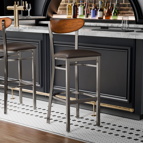 Two Lancaster Table & Seating Boomerang bar stools with dark brown vinyl seats at a wood bar.