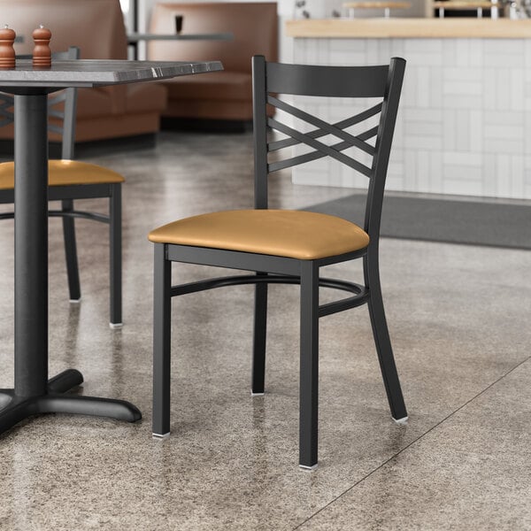 A Lancaster Table & Seating black cross back chair with a light brown cushion on a table in a restaurant.