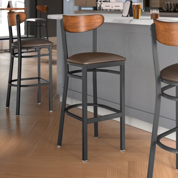 Lancaster Table & Seating Boomerang Series bar stools with dark brown vinyl seats and antique walnut backs at a restaurant counter.