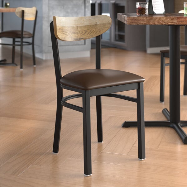 A Lancaster Table & Seating Boomerang chair with a dark brown vinyl seat and driftwood back on a table in a restaurant.