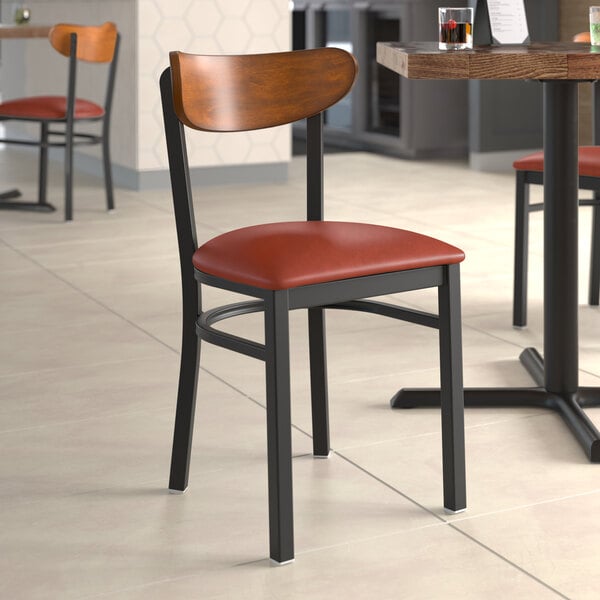 A Lancaster Table & Seating Boomerang chair with a burgundy vinyl seat and antique walnut back on a table in a restaurant.