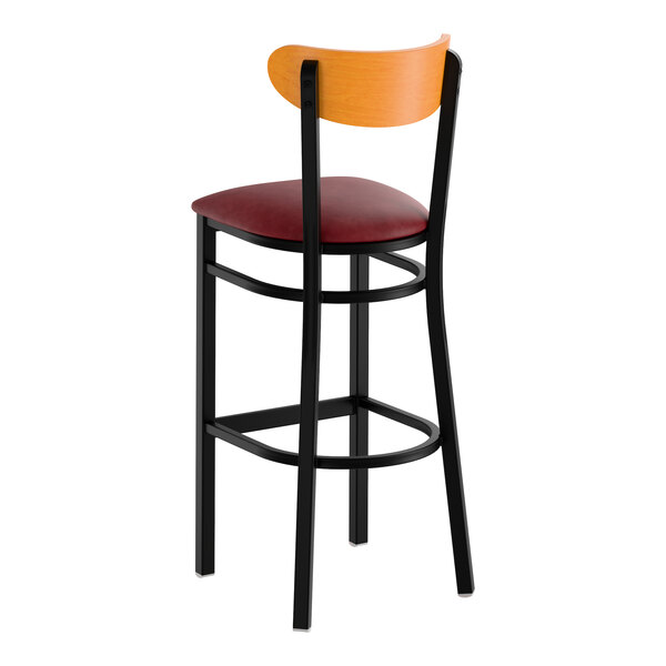 A bar stool with a black metal frame, burgundy vinyl seat, and cherry wood backrest.