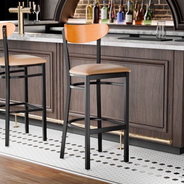 A black bar stool with a light brown vinyl seat and a cherry wood backrest.