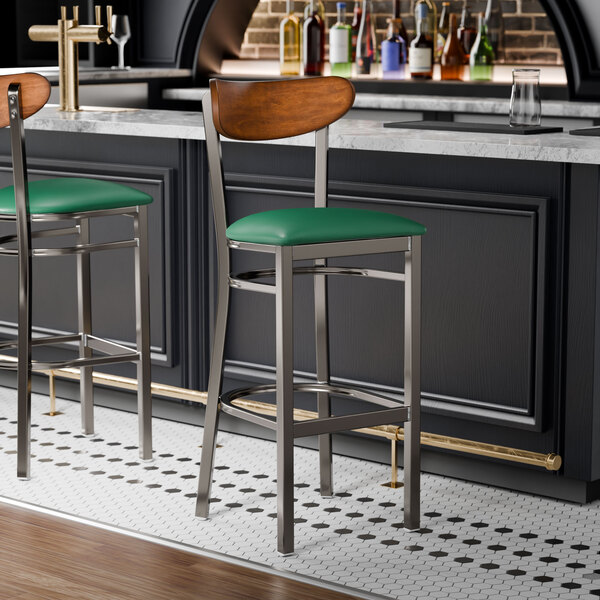 Two Lancaster Table & Seating bar stools with green vinyl seats and wood backs at a black bar counter.