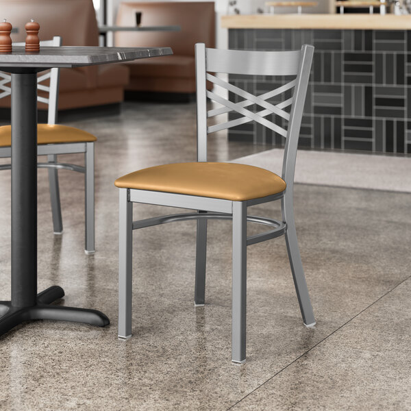 A Lancaster Table & Seating clear coat finish cross back chair with a light brown cushion next to a table in a restaurant.