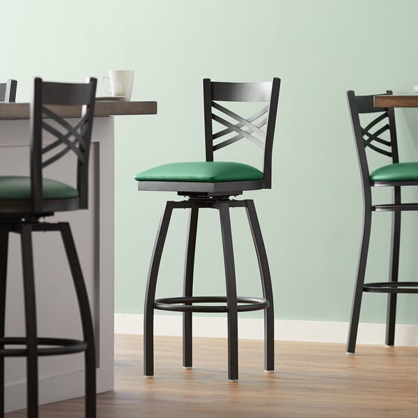 A Lancaster Table & Seating black swivel bar stool with a green cushion.