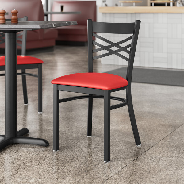 A Lancaster Table & Seating black cross back chair with a red vinyl padded seat at a table in a restaurant.