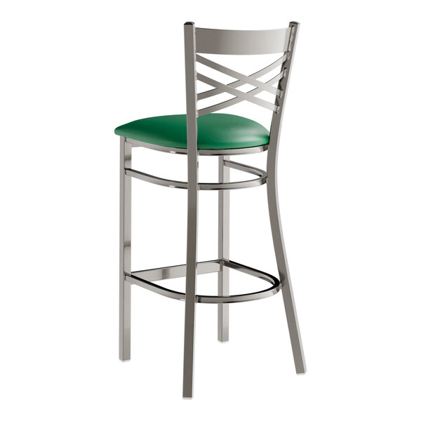 A metal bar stool with a cross back design and a green vinyl padded seat.