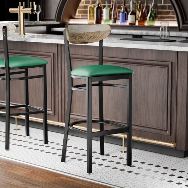 A bar stool with a black metal frame, green vinyl seat, and a driftwood-finished wooden backrest.