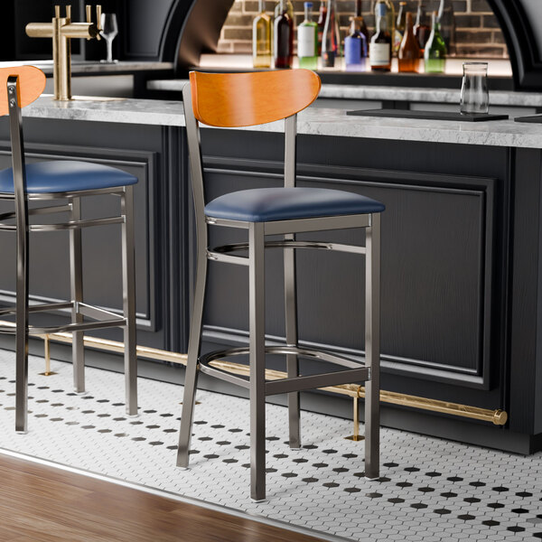 Two Lancaster Table & Seating Boomerang bar stools with navy seats and cherry wood backs at a black counter.