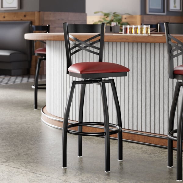 A black metal bar stool with a cross back design and a burgundy vinyl padded seat.