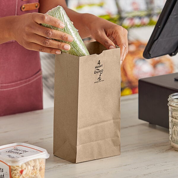 A woman putting a Duro Husky brown paper bag into a paper bag at a register.