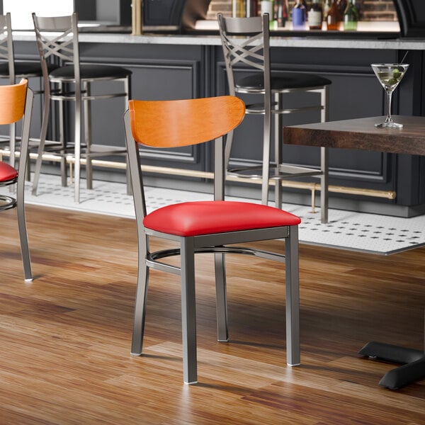 A metal chair with a red vinyl seat and a cherry wood backrest.