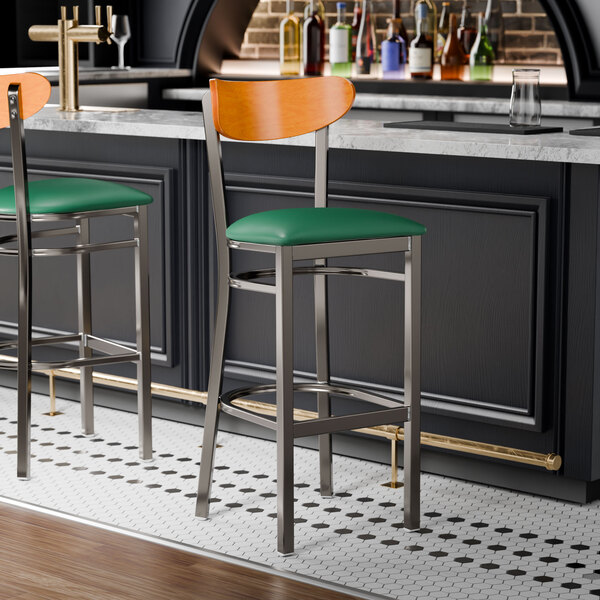 Two Lancaster Table & Seating bar stools with green vinyl seats and cherry wood backs at a black counter.