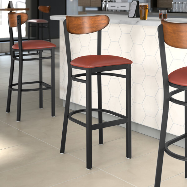 Three Lancaster Table & Seating Boomerang Series bar stools with burgundy vinyl seats and antique walnut backs at a restaurant counter.