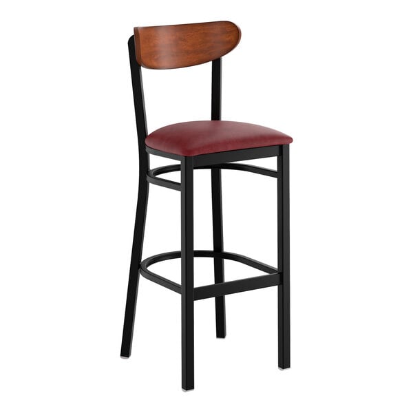 A bar stool with a black metal frame, burgundy vinyl seat, and an antique walnut wood backrest.