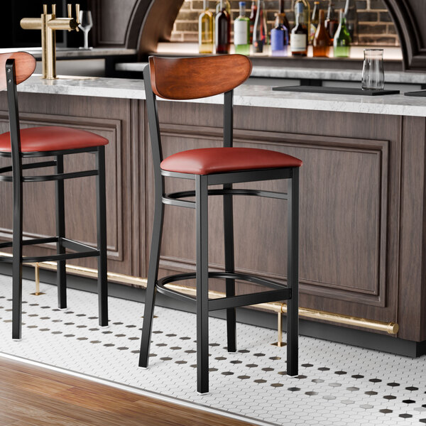 A bar stool with a black metal frame, burgundy vinyl seat, and an antique walnut wood backrest.
