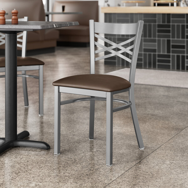 A Lancaster Table & Seating clear coat finish cross back chair with a dark brown vinyl padded seat at a table in a restaurant.