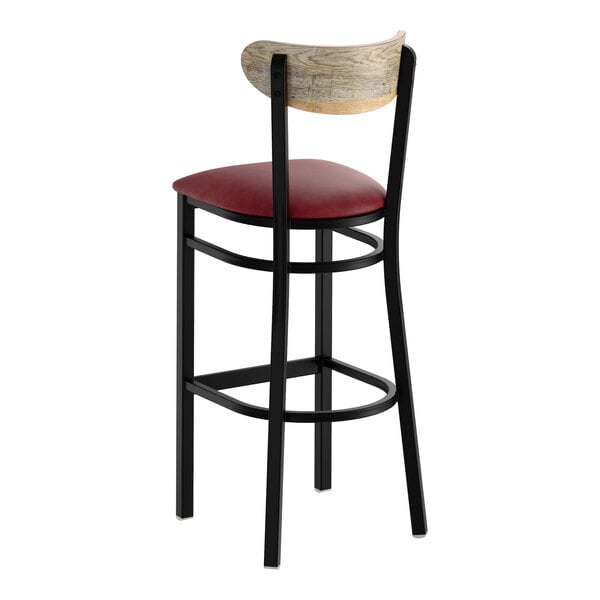 A bar stool with a black metal frame, a burgundy vinyl seat, and a driftwood-finished curved wooden backrest.