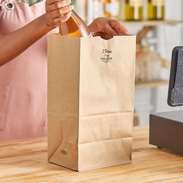 A person opening a Duro brown paper bag with a glass bottle of liquid inside.