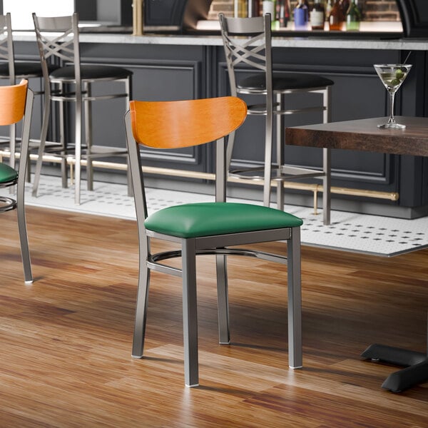 A metal chair with a green vinyl seat and a cherry wood backrest.