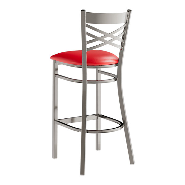 A metal bar stool with a cross back design and a red vinyl padded seat.