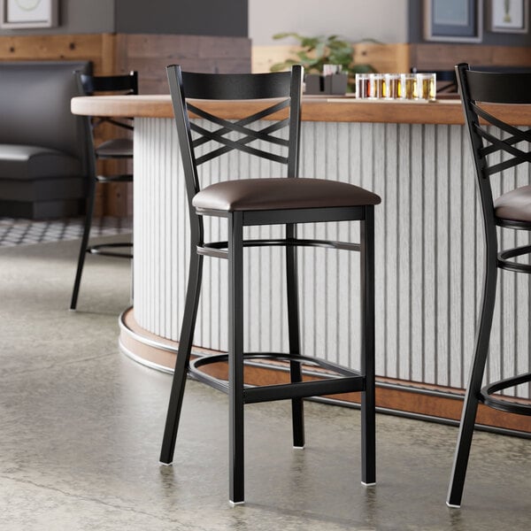 A black metal bar stool with a cross back design and a dark brown vinyl padded seat.