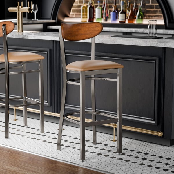 Two Lancaster Table & Seating bar stools with wood backs and light brown vinyl seats at a bar counter.