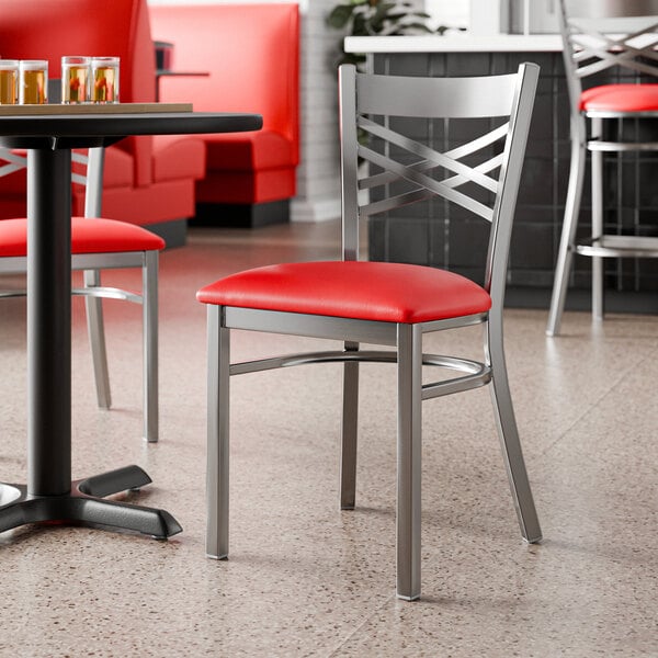 A metal chair with a cross back design and a red vinyl padded seat.