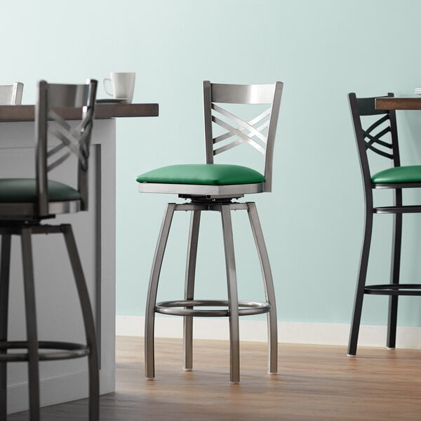 A Lancaster Table & Seating clear coat finish swivel bar stool with a green cushion.