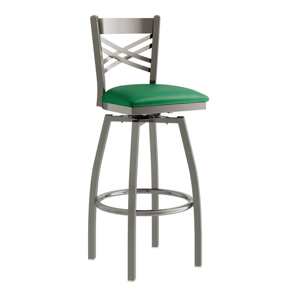 A Lancaster Table & Seating clear coat metal cross back swivel bar stool with a green vinyl padded seat.