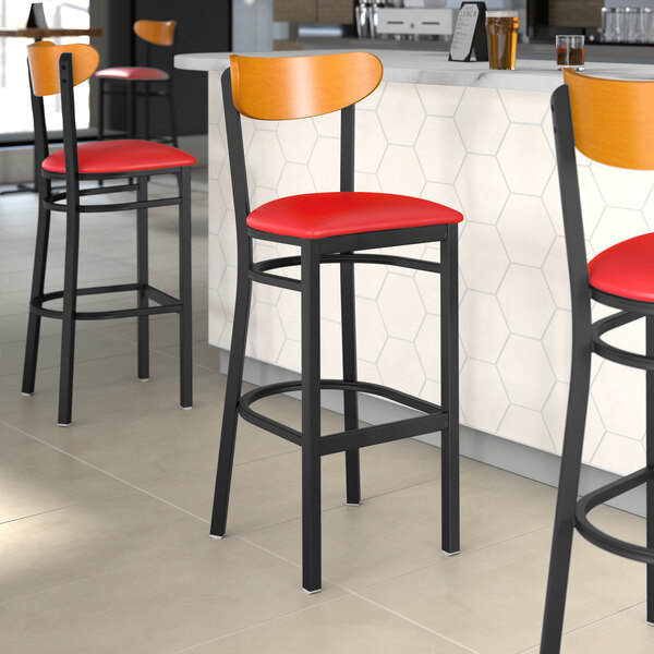 A Lancaster Table & Seating black bar stool with a red vinyl seat and cherry wood back.