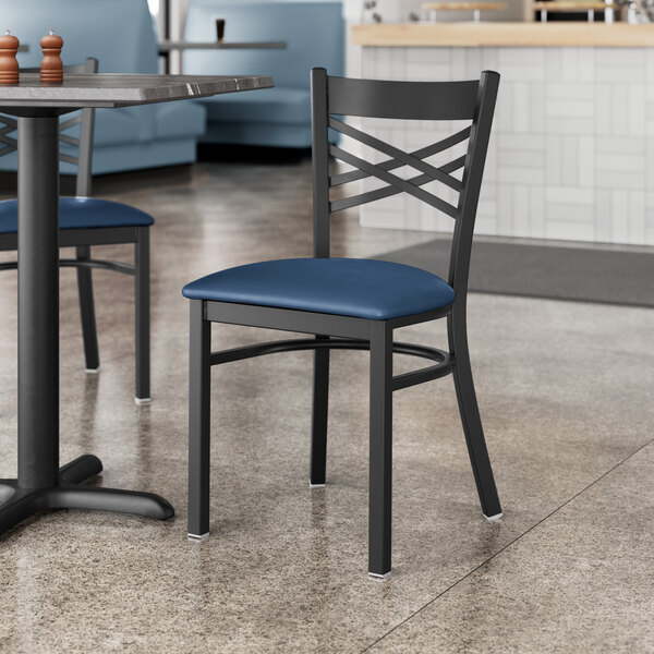 A pair of Lancaster Table & Seating black cross back chairs with navy cushions on a table in a restaurant.