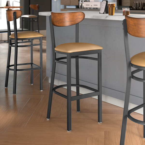 Lancaster Table & Seating Boomerang Series bar stools with light brown vinyl seats and antique walnut wood backs at a restaurant counter.