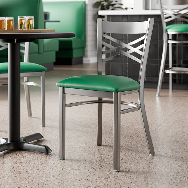 A metal chair with a cross back design and a green vinyl padded seat.
