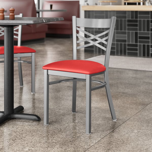 A Lancaster Table & Seating clear coat finish cross back chair with a red vinyl padded seat at a table in a restaurant.