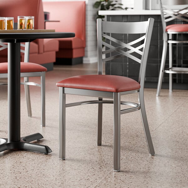 A metal chair with a cross back design and a burgundy vinyl padded seat.
