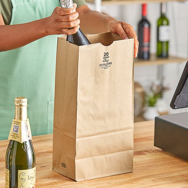 A hand pouring wine from a bottle into a brown paper bag.