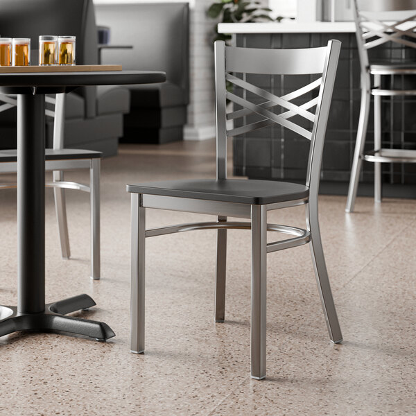 A metal cross back chair with a clear coat finish and a black wood seat.