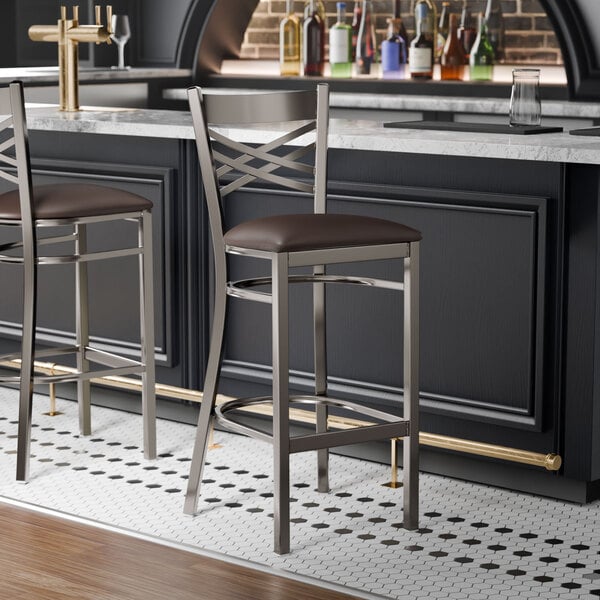 A metal bar stool with a cross back design and a dark brown padded vinyl seat.