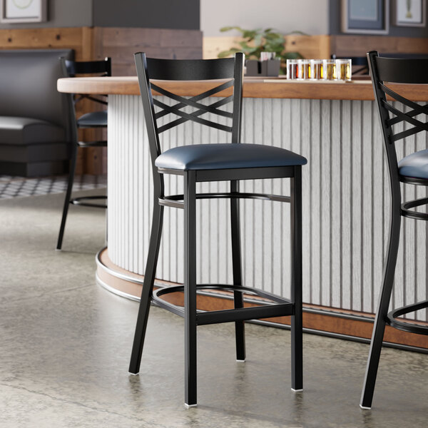 A black metal bar stool with a cross back design and a navy blue padded vinyl seat.
