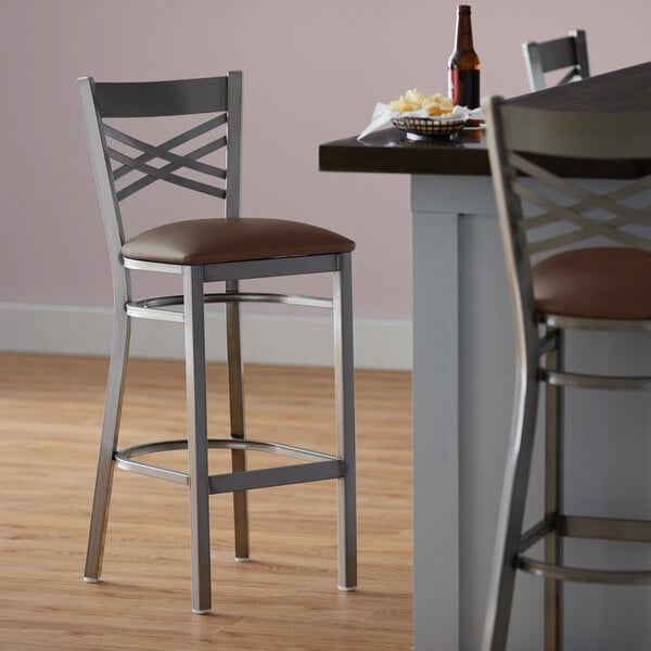 A Lancaster Table & Seating cross back bar stool with a dark brown vinyl padded seat.