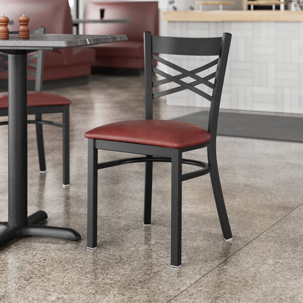 A Lancaster Table & Seating black cross back chair with a burgundy cushion on a table in a restaurant.