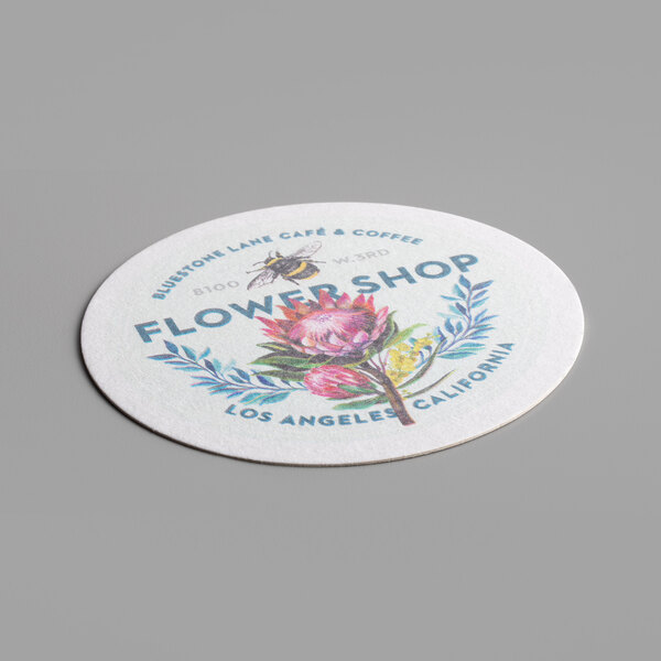 A close-up of a white round coaster with a flower and a bee on it.