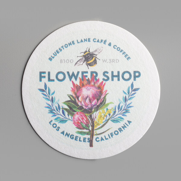 A white round paper coaster with a flower and a bee on it.