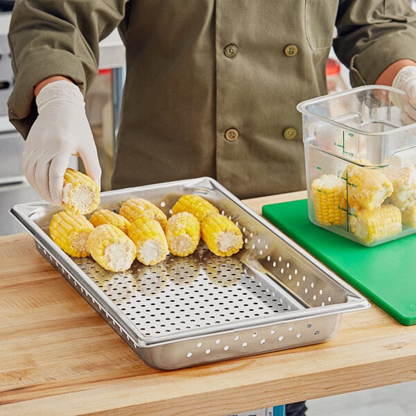 A person in a chef's uniform using a Vollrath stainless steel tray to serve corn on the cob.