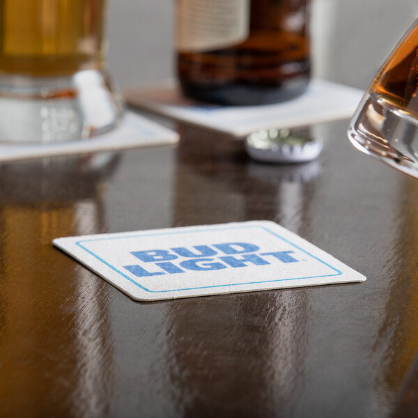 A white square paper coaster with a glass of beer on a table.