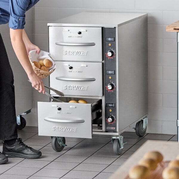 A stainless steel mobile triple narrow freestanding drawer warmer with three drawers and control knobs, used for keeping food warm.